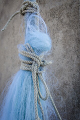 Una rete da pesca stesa ad asciugare ad un muro grigio e tenuta legata con una corda