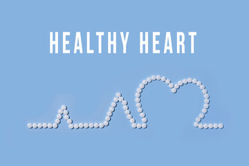 Medicine, healthcare and pharmacy concept - pills and of drugs in shape of the heart and heart rhythms with text Healthy heart on blue backgraund