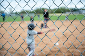 Selective focus on chain link fence with a youth baseball game defocused and blurred in the background