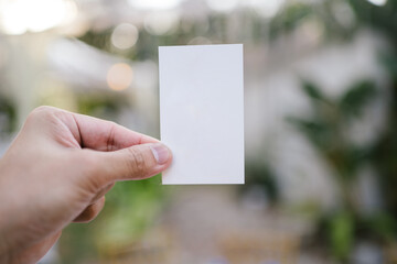 Hand holding a white card with the garden dinner blurry background