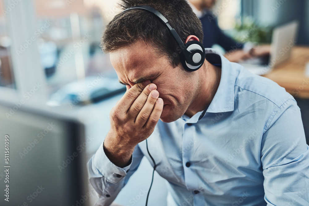 Poster its been a long workday. shot of a young call centre agent looking stressed out while working in an 