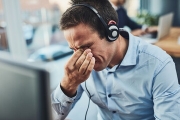 Its been a long workday. Shot of a young call centre agent looking stressed out while working in an...