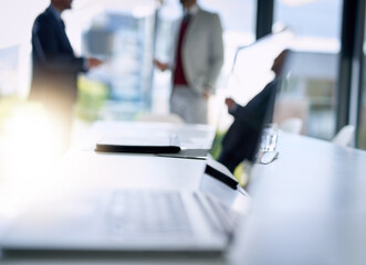 Business in focus. Shot of an open laptop on a boardroom desk with two businessmen blurred in the background.
