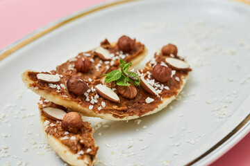 Bananas with peanut butter, almonds and nuts, on wood plate on white plate. Healthy food. Close up