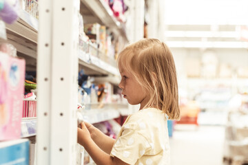 Little caucasian girl choosing a new toy in the big baby store. Big shelfs full of toys