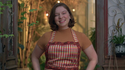 Fototapeta premium Small business store female employee portrait standing inside local shop smiling at camera wearing apron