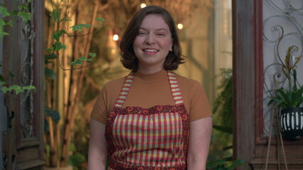 Naklejka premium Small business store female employee portrait standing inside local shop smiling at camera wearing apron