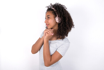 Fototapeta na wymiar Young beautiful girl with afro hairstyle wearing grey t-shirt over white wall wears stereo headphones listening to music concentrated and looking aside with interest.