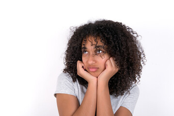 Portrait of sad Young beautiful girl with afro hairstyle wearing grey t-shirt over white wall hands face look empty space