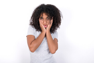 Fototapeta na wymiar Young beautiful girl with afro hairstyle wearing gray t-shirt over white background keeps hands on cheeks has bored displeased expression. Stressed hopeless model