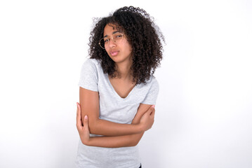Young beautiful girl with afro hairstyle wearing gray t-shirt over white background shaking and...