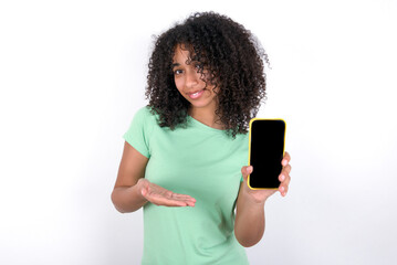 Young beautiful girl with afro hairstyle wearing green t-shirt over white background with a mobile. presenting smartphone. Advertisement concept.