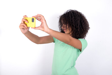 Young beautiful girl with afro hairstyle wearing green t-shirt over white background taking a...