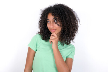 Fototapeta na wymiar Thoughtful Young beautiful girl with afro hairstyle wearing green t-shirt over white background holds chin and looks away pensively makes up great plan