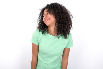 Positive Young beautiful girl with afro hairstyle wearing green t-shirt over white background with overjoyed expression closes eyes and laughs shows white perfect teeth