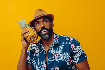 handsome mid adult bearded african american man in Hawaiian shirt posing with pineapple as...