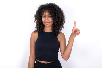 Young beautiful girl with afro hairstyle wearing black tank top over white background showing and pointing up with finger number one while smiling confident and happy.