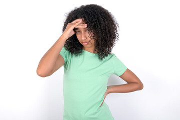 Young beautiful girl with afro hairstyle wearing green t-shirt over white background having problems, worried and stressed holds hand on forehead.