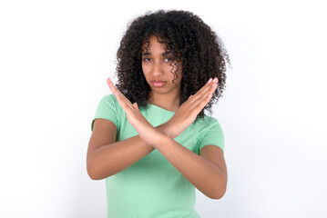 Young beautiful girl with afro hairstyle wearing green t-shirt over white background Rejection expression crossing arms doing negative sign, angry face