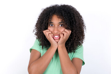 Fearful Young beautiful girl with afro hairstyle wearing green t-shirt over white background keeps hands near mouth, feels frightened and scared,  has a phobia,  Shock and frighted concept.