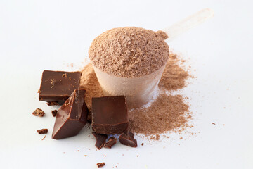 Chocolate Protein powder in Plastic measuring spoon with pieces of brick. dark chocolate isolated on white background Top view.
