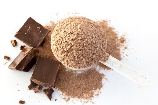 Chocolate Protein powder in Plastic measuring spoon with pieces of brick. dark chocolate isolated on white background Top view.
