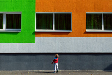 A small boy next to the colored wall of a large building