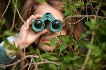 Bird watching is serious. Shot of a cute little girl looking through a pair of binoculars outdoors. - Powered by Adobe