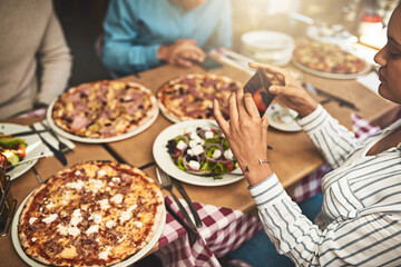 Pizza. Shot of a group of people seated at a table with plates of pizza in front of them while one...