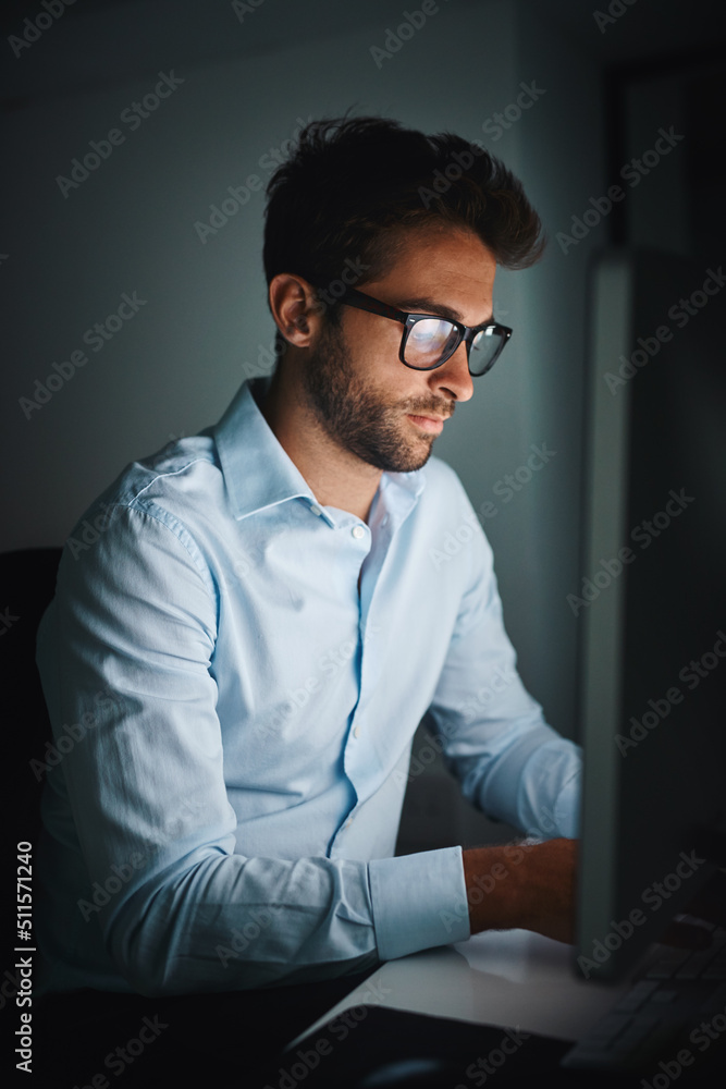 Wall mural Powering through the night to get ahead. Shot of a young businessman working late on a computer in an office.