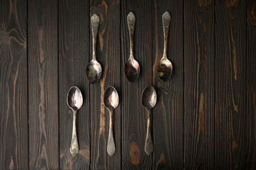 Six old silver spoons on a rustic wooden background.