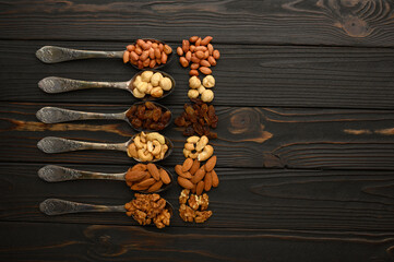 Hazelnut, cashews, raisins, almonds, peanuts, walnuts in silver spoons on a rustic background