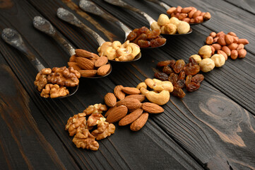Fototapeta premium Hazelnut, cashews, raisins, almonds, peanuts, walnuts in silver spoons on a rustic background