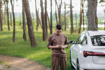 Young attractive smiling man with beard standing near his car and holding mobile phone