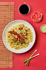 Instant noodles composition. Noodles and fresh vegetables and spices on bright red background