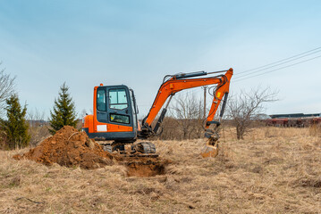 Mini excavator digging earth in a field or forest near roadway.Digging trenches for a gas pipeline or oil pipeline.Spring,autumn blue sky background.