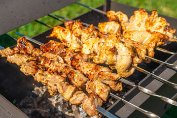 The process of cooking barbecue on a metal grill with burning firewood and smoke.Grilled meat. Cooking for a picnic.Delicious, juicy, aromatic pieces of shashlik.Meadow background.