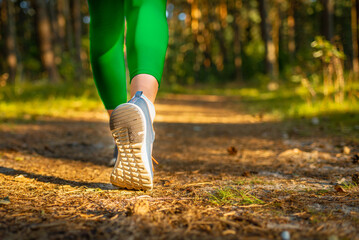 Woman running or walking on nature green blurred background.Health exercise concept.Sunny Nature summer evening park.Closeup.