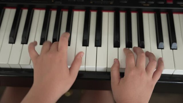 Close up above young girl's hands practicing song on piano in home