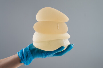 Doctor in a rubber glove holding a pile of breast implants. 