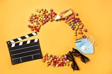 Tasty and colour popcorn, 3d glasses and movie clapper, protective mask on yellow background.