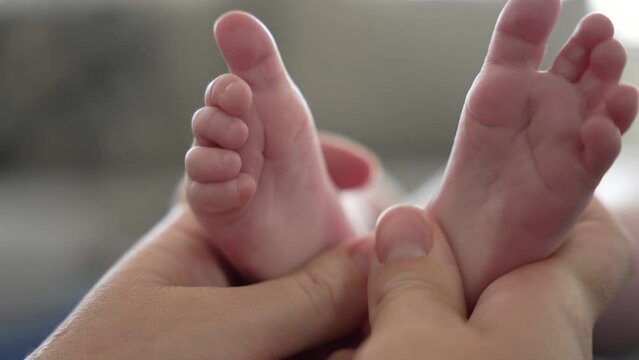 Mother massages newborn infant baby's feet with thumbs tender touch parenting