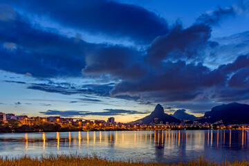 Dusk at Rodrigo de Freitas lagoon with the buildings, hills and lights of the city of Rio de...
