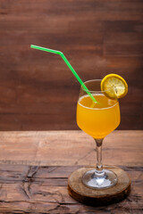 Fruit cocktail with a straw garnished with a slice of lemon in a large glass on a wooden table.