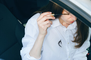 Cosmetic stain on white shirt. Woman applying mascara while sitting in the car