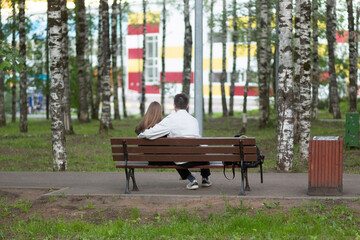 A couple of young people, a girl and a guy are sitting on a park bench.