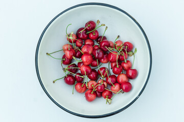 Many red cherry fruits in round bowl, isolated on white. Organic berries fresh. A lot of sweet cherries with petioles top view