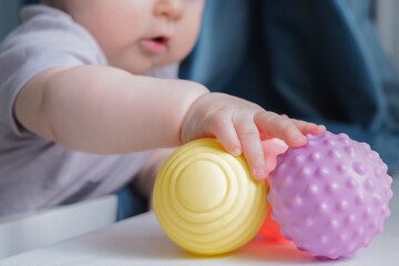 Baby holding a colorful sensory soft ball for babies and kids. Concept of massage textured balls for developing tactile senses.  - obrazy, fototapety, plakaty