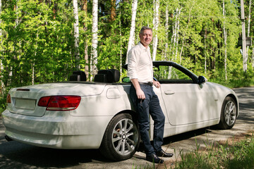 Attractive man next to a cabriolet on the background of the forest