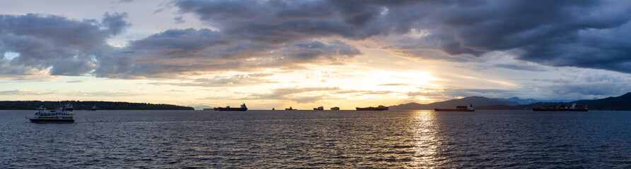 Big Container Ship parked in Burrard Inlet on the West Coast of Pacific Ocean. Colorful cloudy sunset sky. Vancouver, British Columbia, Canada. Panorama Nature Background